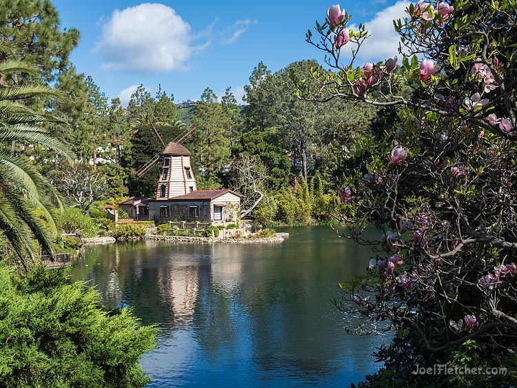 Windmill building on a lakeshore surrounded by pretty trees.